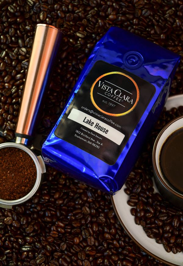 Bag of Vista Clara Lake House coffee surrounded by beans, with a copper grinder and fresh coffee in a cup.