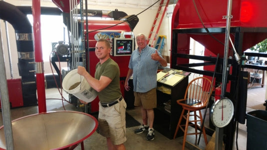 Two men with green and blue shirts stand in a warehouse with red equipment.. 
