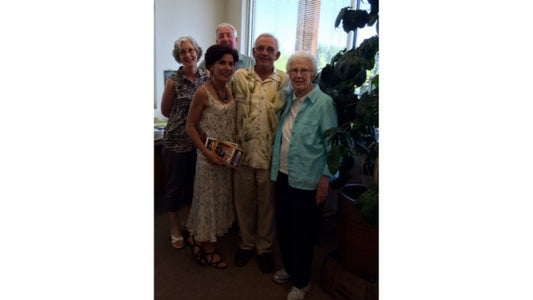 Four people with blue, yellow, and dark shirts standing next to a green plant inside. 
