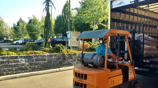 Orange forklift unloading goods with a natural green background.