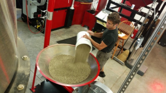 Man in warehouse pouring brown beans into funnel with red background equipment.