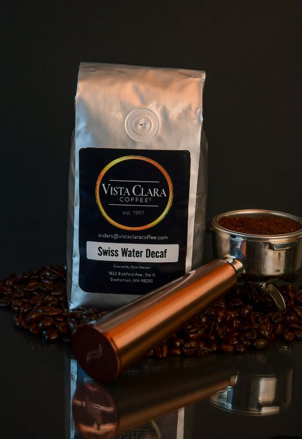 Vista Clara Coffee Swiss Water Decaf bag displayed with a portafilter and ground coffee against a dark background, emphasizing premium decaf coffee quality.